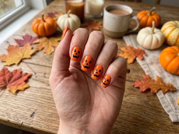 Jack-o'-lantern Halloween nail art on glossy orange square nails with smiling pumpkin faces on both hands.