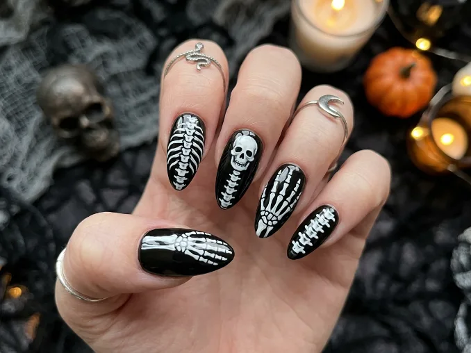 Skeleton bone Halloween nail art on glossy black coffin nails with white bone designs on both hands.